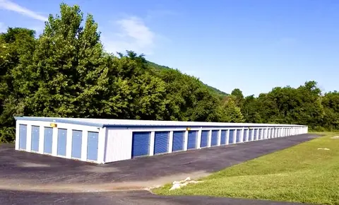 Long white self storage building with blue roll-up doors on a paved drive, backed by trees and Shenandoah Valley hills