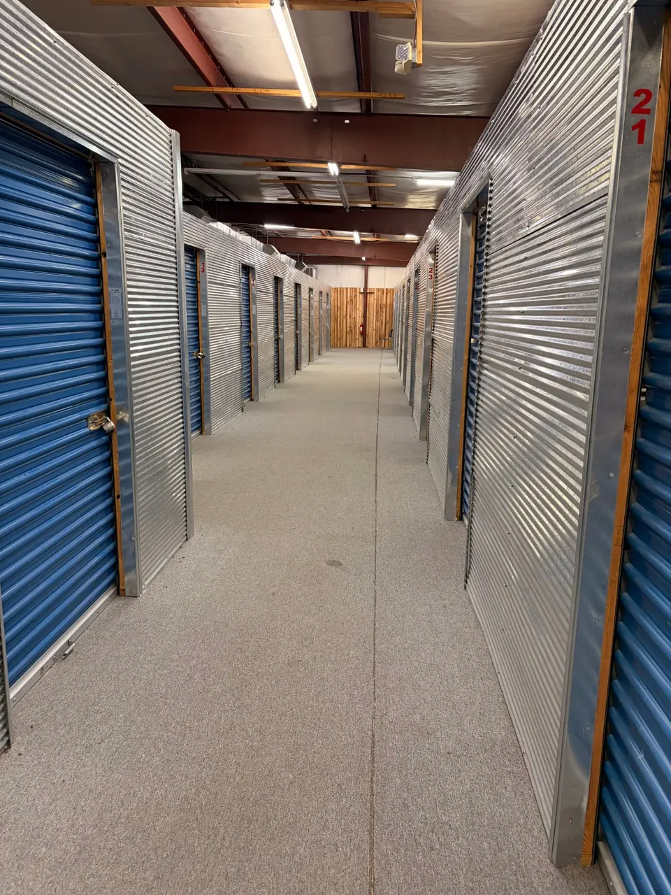 Wide indoor hallway of climate-controlled storage units with blue roll-up doors and wood-partition walls in Staunton, Virginia, serving Mint Spring, VA
